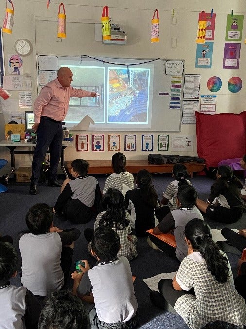 Teacher pointing to electronic whiteboard while group of students sitting on floor look at the board.