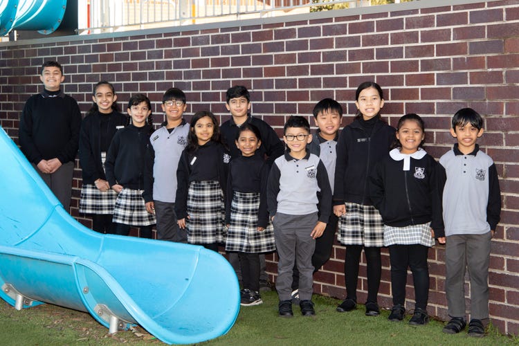 Line of students standing next to blue cylindrical slippery dip in front of a brick wall