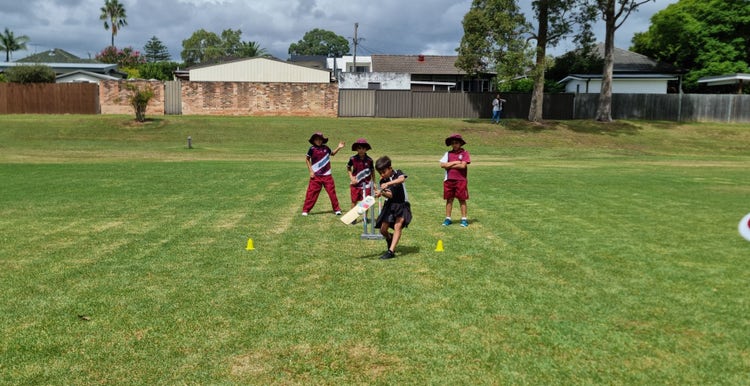 Group of students playing cricket on sports field