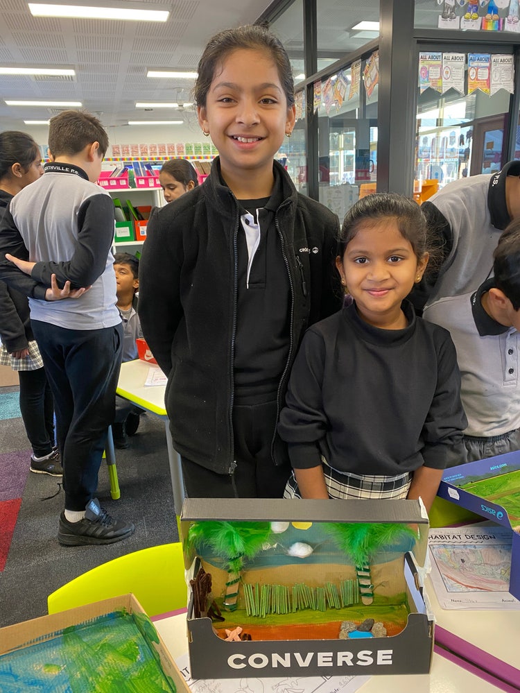 Two smiling female students with project in cardboard box