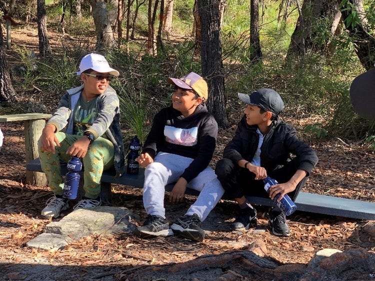 Three male students wearing caps sitting outside under trees